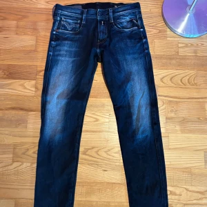 Mörkblå Replay jeansbyxor herr - Säljer ett par mörkblå Replay anbass jeans med klassisk femficksdesign och raka ben. Byxorna har snygga slitningar och Replay-logga på fickan. Midjemått W29 och längd L30. Perfekta för dig som gillar stilrena jeans med bra passform.