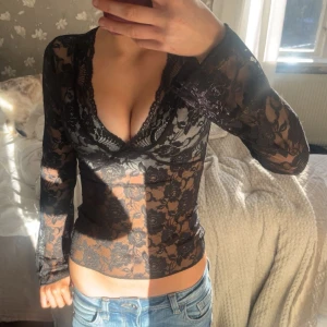 Svart spetsblus med v-ringning - Säljer en svart, transparent spetsblus med v-ringning och långa ärmar. Blusen har ett blommigt spetsmönster och sitter tight. Perfekt för dig som vill ha en trendig och snygg topp till din outfit. PRISLAPP SITTER KVAR