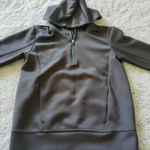 Din tjock tröja bra condition  - Mörkgrå/svart hoodie från Lindex med huva och halv dragkedja framtill. Tröjan har långa ärmar och är tillverkad i ett mjukt syntetmaterial. Perfekt för kyligare dagar och enkel att dra på sig.