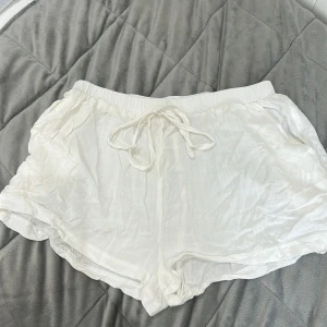 Vita linneshorts med snörning - Säljer ett par vita shorts i linne med elastisk midja och snörning framtill. De har en avslappnad passform och är perfekta för varma dagar. Lätta och luftiga med diskreta fickor i sidorna.