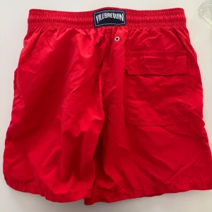 Röda badshorts från Vilebrequin M - Snygga röda badshorts från Vilebrequin med elastisk midja, snörning och bakficka med lock. Klassisk design med broderad sjöhäst på benet och meshfoder. Perfekta för stranden eller poolen. Nypris 1500kr