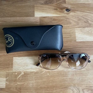 Ray Band - Säljer ett par Ray-Ban solglasögon med pilotformade bågar i transparent beige plast och bruna tonade glas. Klassisk Ray-Ban-logga på linsen och svart fodral medföljer. Modell RB2198 Bill.