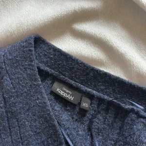 Mörkblå ribbad kofta från KappAhl - Mysig mörkblå kofta från KappAhl i ribbstickat material. Koftan har v-ringning, tre knappar framtill och långa ärmar. Knappt använd och inte speciellt sliten.