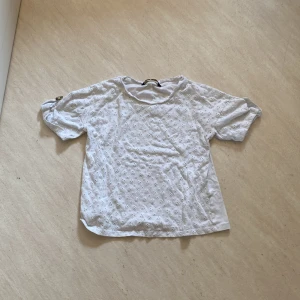 Vit blus med broderade blommor - Säljer en söt vit blus med broderade blommor och korta ärmar. Ärmarna har knappdetalj som ger en extra touch. Perfekt till sommaren och enkel att matcha med jeans eller kjol.