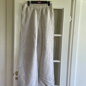 Beiga vida linnebyxor med dragsko - Säljer ett par ljusbeiga linnebyxor med bred passform och dragsko i midjan. Byxorna har en avslappnad look och är perfekta för varmare dagar. Materialet är svalt och luftigt linne.