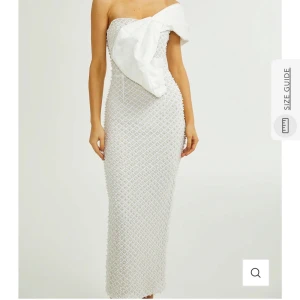 Vit axelbandslös långklänning med stor rosett - Superfin vit axelbandslös långklänning med en stor rosett framtill och pärlbroderier över hela klänningen. Köpt från miss rosier för 2300 kronor. Alla pärlor sitter på plats. Säljer för 1500 men pris kan diskuteras vid snabbt köp. Storlek M.