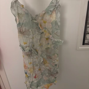 Blommig volangklänning från HM - Säljer en söt blommig klänning i pastellfärger med volangdetaljer och omlottkänsla. Klänningen är ärmlös med smala axelband och har en lätt och luftig känsla, perfekt för varma dagar. Skriv för fler bilder!!