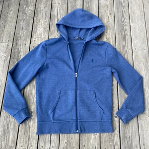 Blå hoodie från Polo Ralph Lauren - Blå Ralph Lauren hoodie i Mycket bra skick! Tröjan är i storlek M och passar ca 175-180 cm! Tröjan är lite smått nopprig på vissa ställen men det syns inte mycket som man kan se på bilderna, Hör av er om frågor!