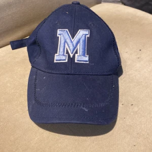 Mörkblå keps med broderat M - Snygg mörkblå keps från GAP med ett stort broderat M i vitt och ljusblått framtill. Justerbar rem baktill för perfekt passform. Klassisk böjd skärm och ventilerande öljetter på ovansidan. Perfekt accessoar för en sportig look.