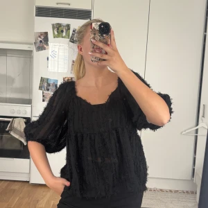 Svart blus med struktur - Säljer en svart, luftig blus med transparent tyg och strukturdetaljer. Blusen har vida trekvartsärmar och en lös passform med lätt v-ringad hals. Perfekt för dig som gillar trendiga och unika plagg.