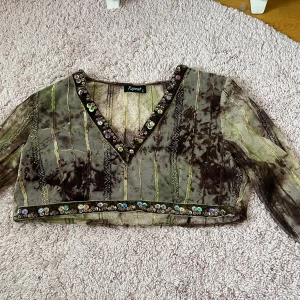 Avklippt topp från Repeat - Säljer en unik transparent croppad topp från Repeat i gröna och bruna toner. Toppen har v-ringning och är dekorerad med paljetter längs halsringning och nederkant. Långa ärmar och broderade detaljer ger en cool look. Jag köpte denna secondhand för några år sedan och klippte av den så att den nu är mer av en croptop.