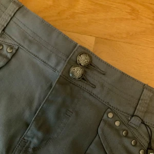 Grå kjol med nitar och dubbla knappar y2k  - Snygg grå kjol från Dr. Denim med dekorativa nitar på fickorna och två mönstrade knappar i midjan. Kjolen har fickor fram och bak samt markerade sömmar för en cool look. Den har fina detaljer, lite y2k liknande kjol. Gullig och har prislappen kvar.