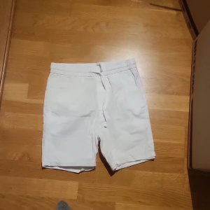 Vita shorts med snörning - Ett par shorts i linne dom har elastisk midja med snörning och sidofickor samt en bakficka. Perfekta för sommardagar och enkel stil.