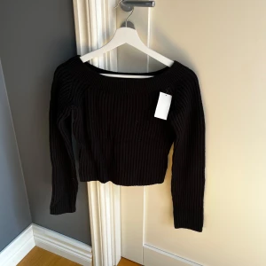 Svart ribbad stickad tröja från H&M - Säljer en svart ribbad stickad tröja från H&M med bred rund halsringning och långa ärmar. Tröjan är croppad och har en klassisk, enkel design som passar till mycket. Perfekt för alla dagar! Prislappen är kvar!!
