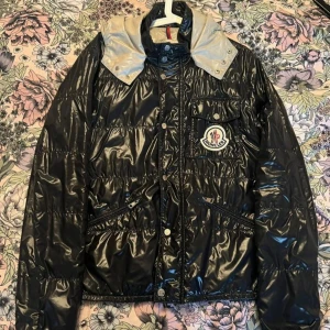 Svart glansig dunjacka från Moncler - Tunn (vår-/höst)jacka från Moncler från sent 00-tal. Saknas en knapp men originalknapp att sy på medföljer  Skickar gärna fler bilder om så önskas