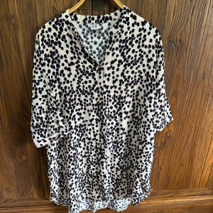 Prickig skjortklänning  - Säljer en luftig skjortklänning med svart och beige prickigt mönster. Klänningen har knappar framtill, trekvartsärm och en lös passform. Perfekt för dig som gillar en avslappnad stil.