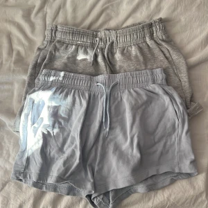 Två par mjuka shorts med dragsko - Säljer två par bekväma shorts med resår och dragsko i midjan. Ena paret är ljusblå och det andra är ljusgrå. Båda har sidofickor och är tillverkade i mjuk bomull, perfekta för sommaren eller träning. Storlek S