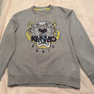 Grå sweatshirt med tigerbroderi från Kenzo - Kenzo tröja  Säljer nu min tröja i storlek s skicket är bra utöver att den har fläkas på sig som ej går att få bort. Inga byten, mötes heller ej upp endast postning som gäller vid köp 