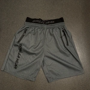 Grå träningsshorts från Gorilla Wear - Snygga grå träningsshorts från Gorilla Wear med svarta detaljer och dragkedjefickor på sidorna. Elastisk midja med logotyp och luftig meshstruktur som passar perfekt för gym eller sport.