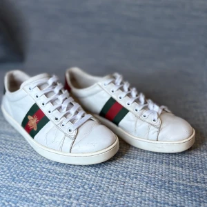 Gucci ace bee - Säljer ett par klassiska vita sneakers från Gucci med gröna och röda ränder på sidorna samt guldbroderad bi-detalj.. Perfekta för dig som gillar stilrena och lyxiga sneakers.