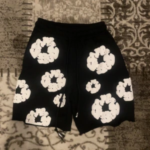 Svarta shorts med vita blommönster - Svarta shorts med stora vita blommönster och snörning i midjan. Shortsen har en normal passform och är tillverkade i ett mjukt material, perfekta för sommaren. Snygg och unik design som sticker ut.