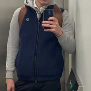 Mörkblå fleeceväst från Morris - Säljer en mörkblå fleeceväst från Morris med dragkedja framtill och ståkrage. Västen har ett diskret Morris-emblem på bröstet och är perfekt för lager-på-lager. Snygg och enkel att matcha till olika outfits.