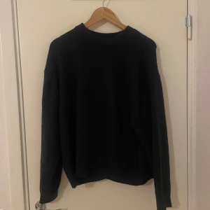 Svart stickad tröja från H&M - En enkel svart stickad tröja från H&M med rund halsringning. Tröjan har långa ärmar och en klassisk passform, perfekt för kyligare dagar. Passar till det mesta och är ett måste i garderoben.