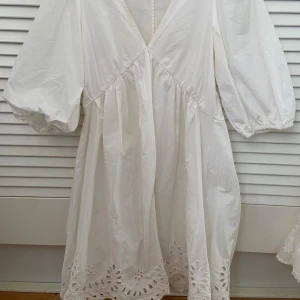 Vit klänning - Vit klänning med v-ringning, trekvartsärmar och broderade blommor längst ner. Passar xs/s!