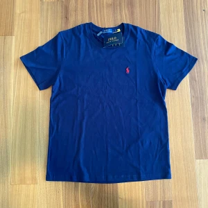 Ralph Lauren T-shirt - Klassisk mörkblå t-shirt från Polo Ralph Lauren med röd broderad logga. Superskön bomull – helt ny med tags kvar!  📏 Storlek: L 🧼 Skick: Ny med etikett 👕 Material: 100 % bomull