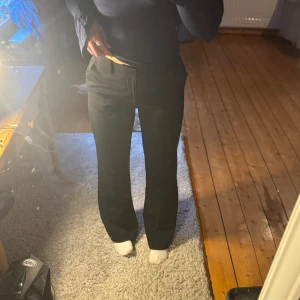 Svarta kostymbyxor från Lindex - Säljer ett par svarta kostymbyxor från Lindex med normal passform och bootcut-stil. Byxorna har hög midja, klassisk dragkedja och knäppning framtill samt sidfickor. Perfekta för en stilren look.