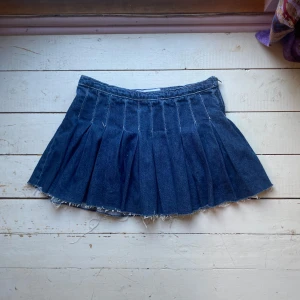 Blå jeanskjol från ZARA - Säljer en blå jeanskjol från ZARA i kort modell med plisserad design och rå, fransig fåll. Kjolen har en cool och avslappnad vibe, perfekt för dig som gillar denim och vill ha något trendigt i garderoben.