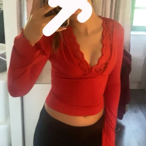 Röd spets topp - Säljer en röd omlottopp med v-ringning och fina spetsdetaljer längs urringningen. Toppen är croppad och har långa ärmar. Perfekt för dig som vill ha något snyggt och trendigt!
