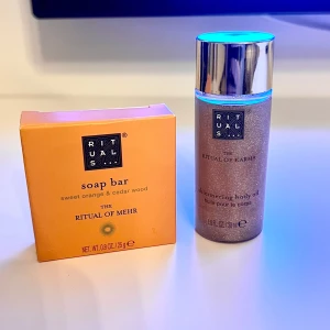 Rituals Shimmering Body Oil & Soap Bar - Shimmering body oil från Ritual of Karma med silvrig glans och en tvålbar från Ritual of Mehr med doft av sweet orange & cedar wood. Oljan kommer i en genomskinlig flaska med silverlock, tvålen i en orange ask. Rituals soap bar 25g Rituals shimmering body oil 30ml