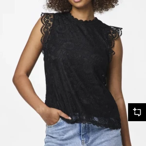 Svart spetsblus med ärmlös design - Säljer en svart ärmlös blus med vacker spets och fina detaljer vid axlarna. Blusen har hög hals och romantiska spetskanter som ger en elegant look. Perfekt att styla med jeans eller kjol.