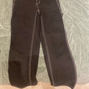 Svarta cargopants med vita sömmar - Säljer ett par svarta cargopants med kontrasterande vita sömmar och flera stora fickor framtill och på sidorna. Byxorna har en loose passform och raka ben, perfekta för en avslappnad streetstil.