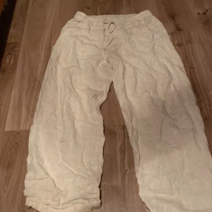 Beige linnebyxor med resår och knyt - Säljer ett par beige linnebyxor med resår i midjan och knytband. Byxorna har en avslappnad passform och raka ben, perfekta för varma dagar. Lätta och luftiga, passar till många olika stilar.