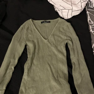 Olivgrön ribbad långärmad tröja från Amisu - Snygg olivgrön ribbad tröja från Amisu  med v-ringning och lång ärm. Perfekt att styla till jeans eller kjol. Mjuk och stretchig i materialet. Lite tajt i midjan viker gör den ännu snyggare och väldigt elegant. Har bara testat den en gång, inte använd så forfarande väldigt bra skick 
