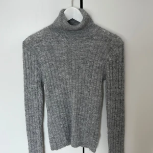 Grå ribbad polotröja från BikBok - Säljer en grå ribbstickad polotröja från BikBok i storlek XS. Tröjan har lång ärm och hög polokrage, perfekt för kyligare dagar. Mjuk och skön kvalitet som passar till många olika outfits.