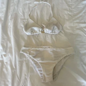 Bikini - Snygg vit bikini med vågigt mönster och gulddetalj mellan kuporna. Säljer pga att de blivit förstora. Båda delarna i strl M. Använd 2 gånger. 