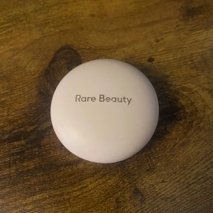 Rare Beauty Joy Powder Blush - Säljer ett puderblush från Rare Beauty i nyansen Joy. Färgen är en varm persiko-orange ton som ger kinderna en fräsch och naturlig lyster. spegel i locket använd 1 gång 