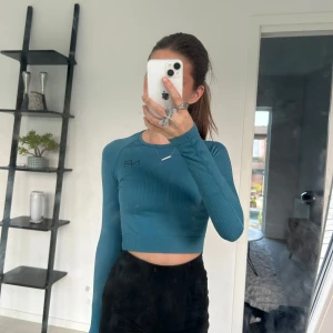 Turkos croppad träningstopp - Säljer en skitsnygg turkos ribbad croppad långärmad träningstopp. Toppen har en tight passform och en liten logga på bröstet. Perfekt till typ gymmet eller idrotten. Hittar inte storleken men skulle tro XXS-XS
