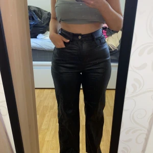 Svarta skinnbyxor med hög midja - Säljer ett par svarta skinnbyxor med hög midja och raka ben. Byxorna har klassisk femficksdesign och stängs med knapp och dragkedja. Perfekta för dig som vill ha en edgy och trendig look.