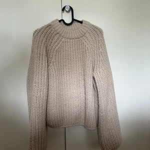 Beige stickad tröja - Säljer en chunky beige stickad tröja med grovstickat mönster och rund halsringning. Tröjan har långa ärmar och är oversize, perfekt för kyliga dagar.