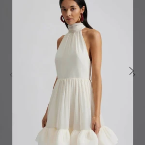 Vit miniklänning med halterneck och volang - Aldrig använd supersöt vit miniklänning med halterneck och knyt i nacken. Perfekt för studenten! Originalpris 3000kr. Prislappen sitter kvar!