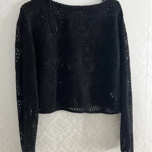 Svart croppad spets-tröja - Säljer en svart långärmad tröja med croppad passform och spetsdetaljer. Tröjan har ett genombrutet mönster som ger en cool och trendig look. Perfekt att styla över ett linne eller topp. tröjan är från lager 157