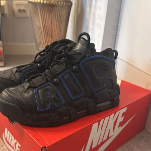 Nike Air More Uptempo svart/blå - Säljer ett par Nike Air More Uptempo i svart med blåa detaljer. Skorna har den ikoniska AIR-texten på sidorna, grov sula och snörning. Perfekta för dig som gillar en chunky sneaker med streetkänsla. Dem är i super bra skick och har bara används 2-3 gånger.