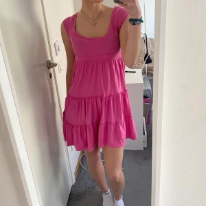 Rosa volangklänning från jsfn - Supersöt rosa klänning från jsfn i storlek 34/36. Klänningen har volanger i flera lager och är ärmlös med rundad urringning. Se bild 4 och 5 för defekter.