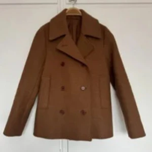 Brun kappa med  krage - Säljer en brun kort kappa med bred krage och dubbelknäppning. Jackan har två stora fickor framtill och en klassisk, rak passform. Perfekt för dig som vill ha en stilren och tidlös look.