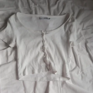 Vit croppad topp med knappar - Säljer en söt vit croppad topp med korta ärmar och knappar framtill. Toppen har en rundad halsringning och är perfekt att matcha med jeans eller kjol.