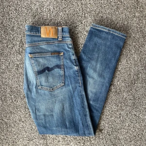 Blå jeans från Nudie Jeans - Säljer ett par snygga blå jeans från Nudie Jeans i bra skick. De har en klassisk femficksdesign och en bekväm passform. Perfekta för både vardag och fest! 🕺storlek 30/30 och modell steaddie Eddie 2. Har dock en lagning i skrevet kolla sista bild men syns inte vid användning 